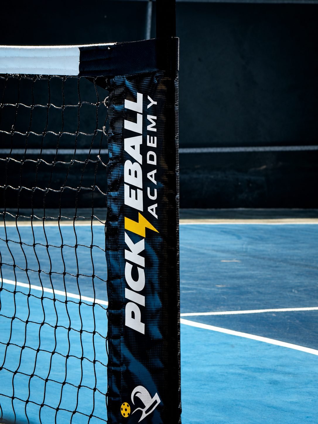 Poste da rede com a marca Pickleball Academy sobre a quadra azul